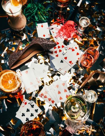 top view of female shoes on high heels, playing cards, alcoholic cocktails and party horns on table